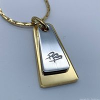 Close-up of pendant and chain showing two-tone trapezoidal dog tag pendant with gold plating and silver plate with PB logo.