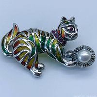 Close-up of cat enamel brooch showing multicolor stripes, ruby eyes, ruby collar stones, marcasite surround and prominent pearl in front paw.