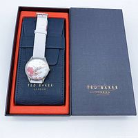 Ted Baker floral quartz watch displayed in navy blue Ted Baker box with orange interior, showing white leather strap and floral dial.