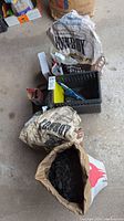 Three opened bags of Cowboy brand charcoal near a plastic basket and BBQ accessories on garage floor.