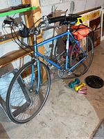 Full view of bicycle leaning against shelving showing frame, tires, handlebars, headlight, weights on floor