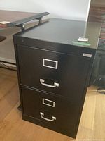 Front view of the black metal filing cabinet showing two drawers with handles and label holders.