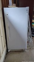 Front view of white Kenmore standing freezer with vertical handle, closed door, showing appliance standing in a garage setting.