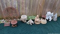 Wide shot showing all garden decor items lined up including cast iron decorative circular panel, two lanterns, stone planter, various frog figures, Buddha and lion stone statues, and smaller stone pieces.