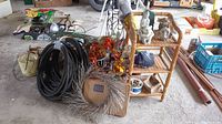 Photo showing wicker three-tier shelf with garden statues, multiple coils of black and green hose, artificial autumn wreath, mesh bags, and various long garden tools.