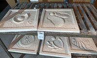 Five garden art tiles arranged on a metal rack, showing all five pieces and their relief designs.