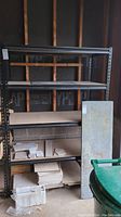 Full view of black metal frame shelving unit with MDF insert shelves and one loose panel leaning beside it.