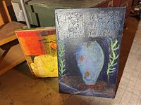 Photo showing two paintings: one with a blue vessel against a dark background and another floral painting with large yellow poppies.