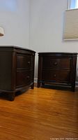 Two dark wood night stands with bowed fronts, two drawers each, wood knobs, standing on hardwood floor.