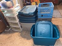 Photo showing Rubbermaid plastic totes blue and grey with lids, a set of white plastic drawers and assorted Tupperware containers on top.