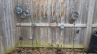Wide view of four metal sunflower garden ornaments mounted on a wooden fence showing varied heights and patina.