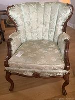 Front view of the chair showing wood carved legs, floral upholstered cushion and tufted backrest.