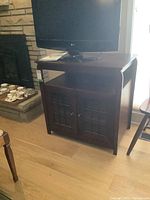 Front view of the dark brown wood veneer TV cabinet with two windowpane-style doors and a flat top with TV set on it.