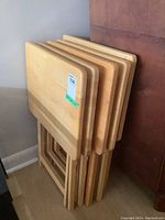 Photo showing 5 stacked light wood folding TV tables with rounded rectangular tops and folding legs.