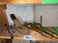 Photo of two vintage brass hose taps, wooden hand planer, and metal art spoon grouped on a wooden shelf.