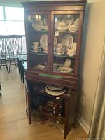 Front view of vintage Pepplers corner china cabinet showing glass doors with shelves containing dishware, middle felted drawer, and bottom wood doors open showing shelf.