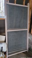 Full view of single large panel with wood frame and wire mesh screen leaning against garage wall.