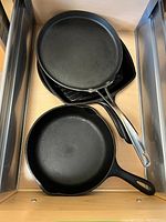 Three cast iron skillets stacked including one with stainless steel handle and two traditional Lodge skillets.
