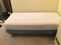 Full bed setup showing mattress with white cover on top of blue box spring and metal frame base.