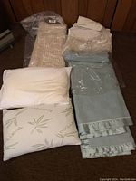 Wide view of all blankets and pillows in the lot showing knitted beige blanket, fleece blankets, and two pillows.