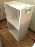 Front perspective view of the white painted book shelf showing its solid rectangular shape and two open shelving compartments.