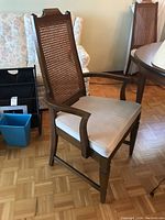 Six cane back dining chairs including one captain chair with wooden frame and off-white seat cushions.