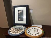 Two framed prints and two round wall clocks with bird motifs on a table against a beige wall