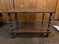 Front view of the rectangular wood veneer coffee table showcasing turned legs and lower shelf on caster wheels against wood panel wall background.