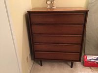 Front view of the vintage wooden dresser showing all five drawers and tapered legs.