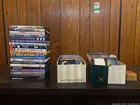 Two boxes containing assorted music CDs alongside a smaller stack of DVDs with visible titles