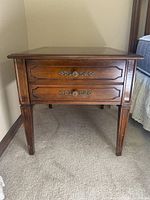Wood end table front view showing two drawers with ornate metal handles and carved wood detailing.