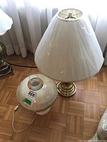 Overview of two vintage lamps, one with beige lampshade and brass base, the other a glass lamp with chimney glass top.