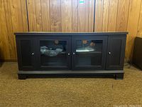 Front view of dark wood veneer media cabinet with glass and solid doors against a wood-paneled wall
