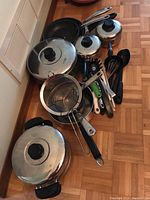 Full view of all pots, pans, and kitchen utensils arranged on floor showing stainless steel cookware and variety of utensils.