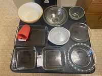 Photo showing all bowls and dishes arranged on a black surface, highlighting a large ceramic mixing bowl with yellow rim, clear glass mixing bowl with lid, Pyrex baking dishes, rectangular and round glass dishes, and a red silicone oven mitt.