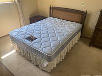 Full view of queen size bed setup with mattress, lace bed skirt, wooden headboard, and base frame in a bedroom.