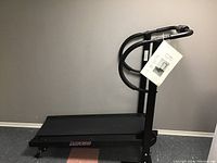 Full view of the black Fit 400 manual treadmill showing the walking deck, handles, and attached user manual.