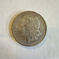 Obverse side of a worn 1902 Morgan silver dollar coin showing Liberty profile and date.