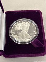 Close-up of the silver coin in protective capsule inside purple velvet case, showing the obverse Walking Liberty design with inscriptions and date 1985.