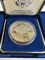 Close-up of silver dollar coin featuring the signing of the U.S. Constitution inside protective capsule and original presentation box interior.