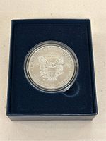 Silver coin featuring the heraldic eagle design on reverse, encased in clear plastic and set in navy blue display box.