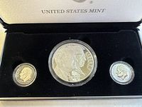 Full view of the three coins in black velvet presentation case with United States Mint marking inside lid. Coins are in protective capsules - large silver dollar in center and two smaller dimes on each side.