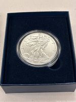 Front view of the 2016 American Eagle silver coin, showing detailed design of Lady Liberty, sealed in clear round case resting in navy blue velvet insert tray.