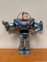 Front view of Buzz Lightyear toy in silver and blue suit, standing upright with arm extended holding a blaster.
