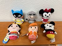 Six small plush toys displayed against a white wall on a wooden surface, representing characters from Disney and Star Wars.