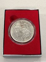 Front side of 1881 Morgan silver dollar coin showing Lady Liberty profile in protective clear case within red foam liner.