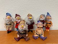 Front view showing all seven dwarves standing and sitting, highlighting assorted colored hats, fabric clothes, and detailed faces with white beards.