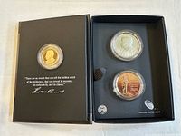 Photo of the open black presentation box displaying three coins in capsules with a quote by Theodore Roosevelt inside the lid.