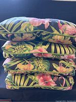 Four stacked tropical patterned patio chair cushions 18x18 inches