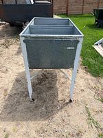 Front view showing galvanized metal washtub with two deep compartments and white metal legs with wheels.